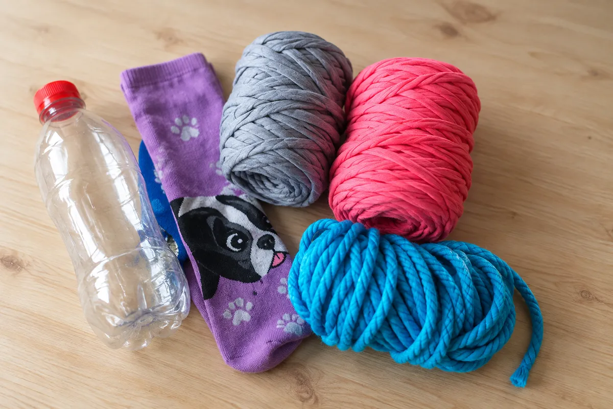 Materials for making homemade dog toys, including a plastic bottle, socks, fabric yarn and rope